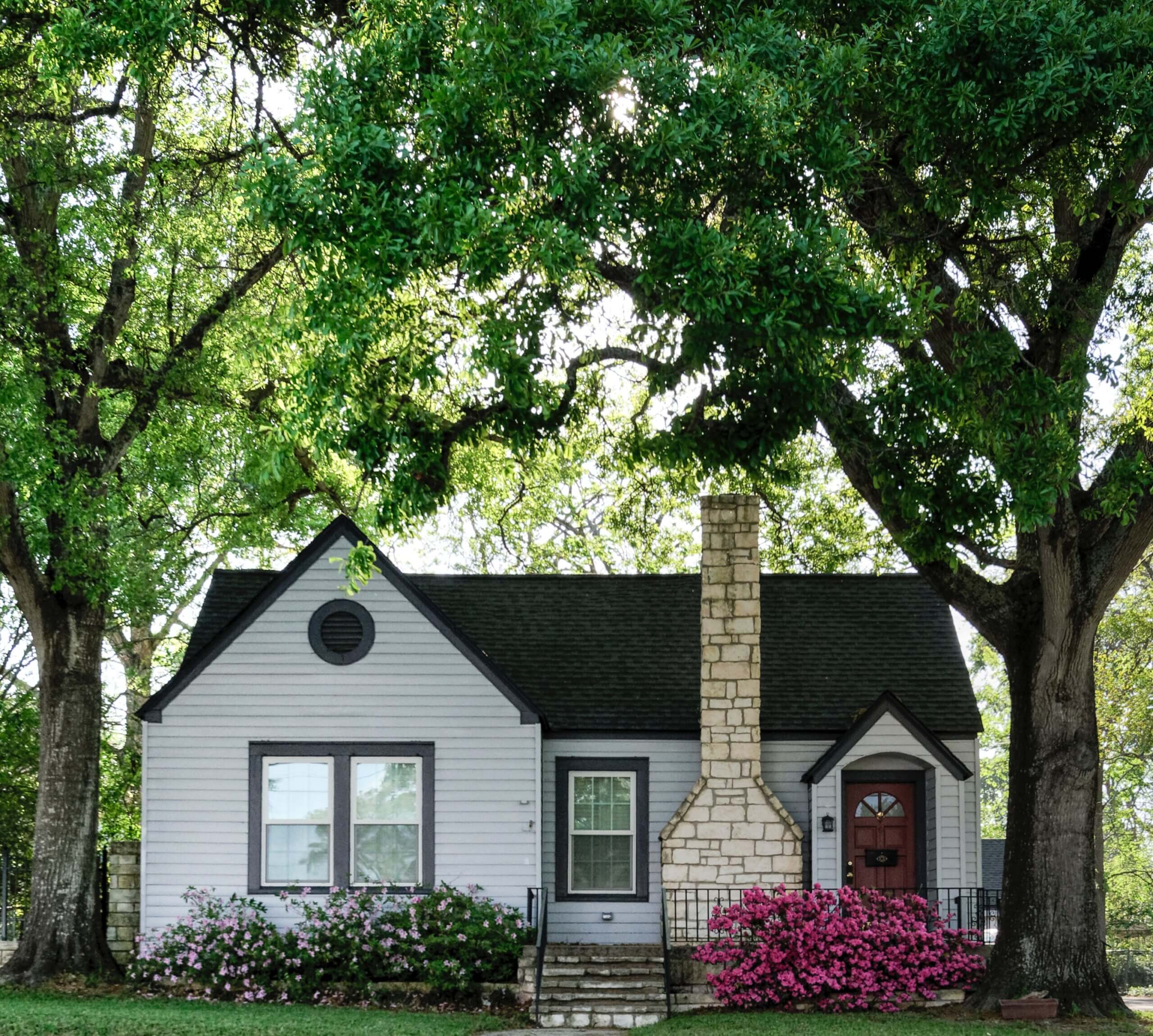 Small gray home with brick chimney and colorful spring flowers.