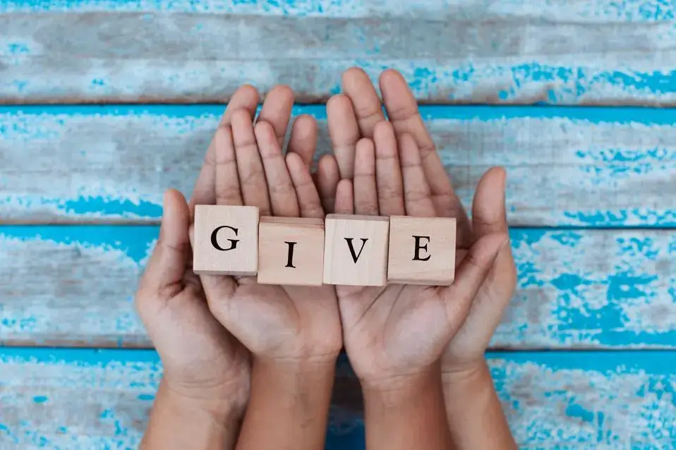 Hands holding wooden blocks that spell out the word "GIVE"